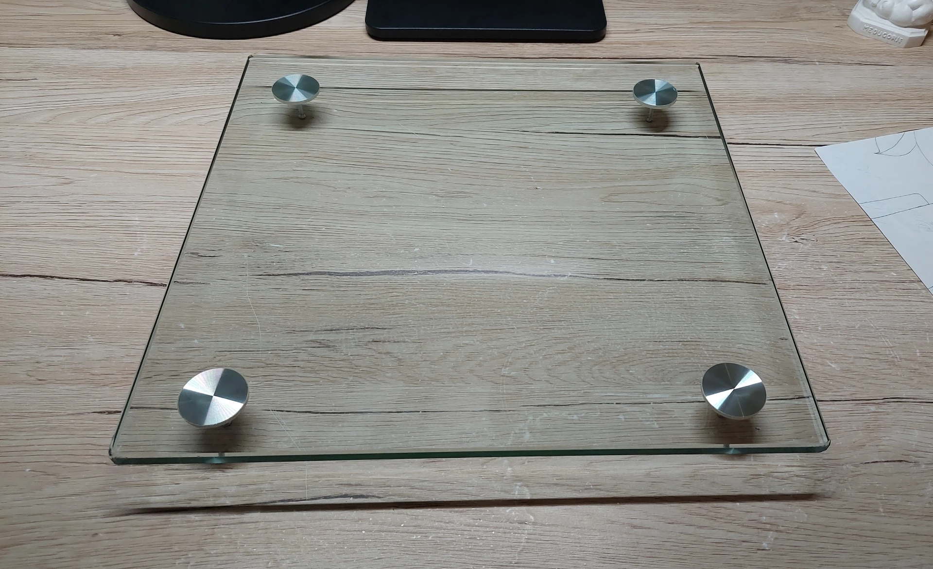 The glass plate from a disassembled bathroom scale, repurposed with four screws as feet to create a DIY light box frame.