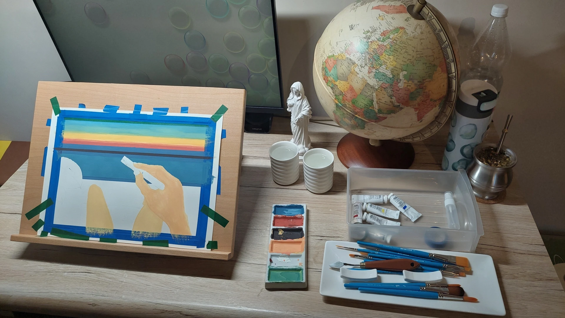 A wider view of the workspace, showing the painting with its background complete on the easel.